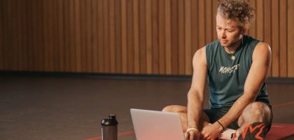 Man sitting on exercise mat with laptop, surrounded by dumbbells, creates a unique fitness workspace.